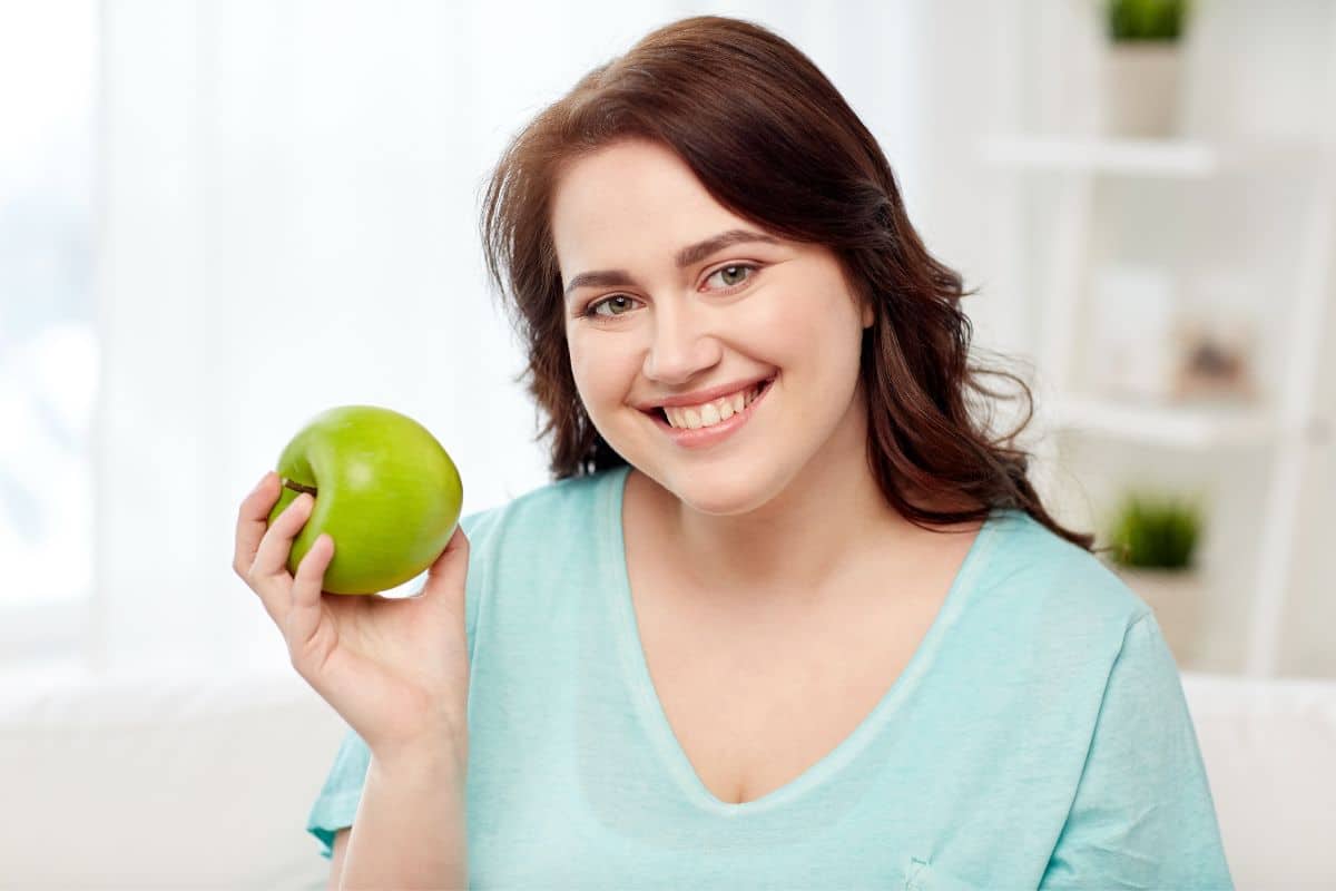 Dieta da maçã: conheça seus benefícios e como fazer 1 Mulher segurando uma mação para iniciar a dieta da maçã.